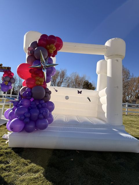 White bounce house with a purple and red balloon garland