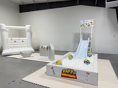 Toy Story-themed ball pit and slide next to a bounce house indoors