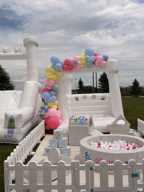 Outdoor bounce house, soft play, and ball pit with a pastel balloon arch