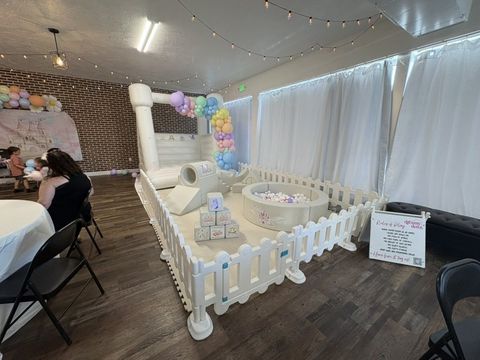 Indoor party with a fenced soft play area, bounce house, and balloon garland