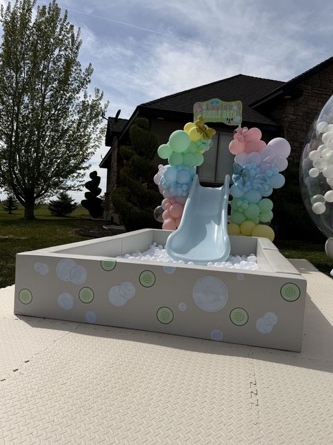 Bubble bath-themed ball pit and slide with a pastel balloon garland