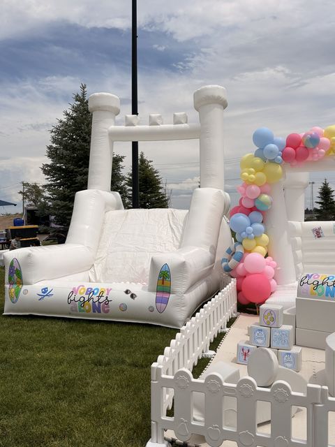 Side view of an outdoor bounce house and soft play set with pastel balloons